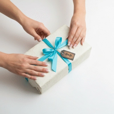 Hands carefully wrapping a gift with elegant paper and ribbon, personal touches like a small tag visible, clean background, no text, no words, no typography, 8K